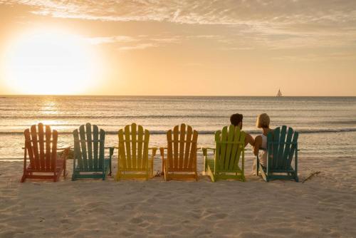 a couple sitting in lawn chairs on the beach at Divi Aruba Phoenix Beach Resort in Palm-Eagle Beach