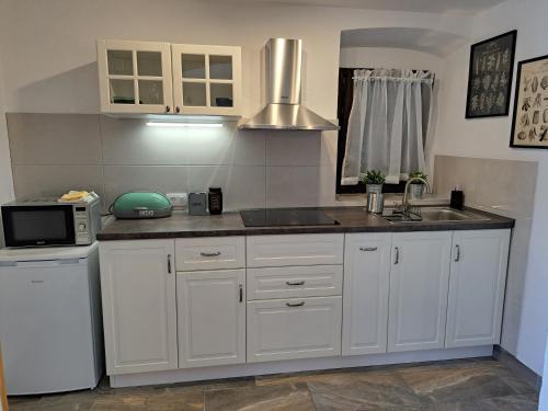 eine Küche mit weißen Schränken, einer Spüle und einer Mikrowelle in der Unterkunft Apartments Dandić in Orlec