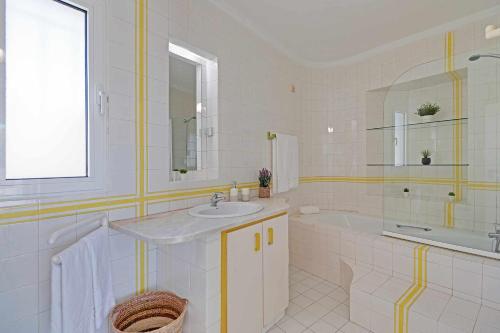 W białej łazience znajduje się umywalka, wanna i lustro. w obiekcie Villux Vila Enar6 quartos ideal para familias w Albufeirze