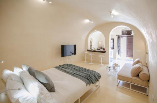 a white bedroom with a bed and a tv at Azalea Houses Cave Villa in Oia