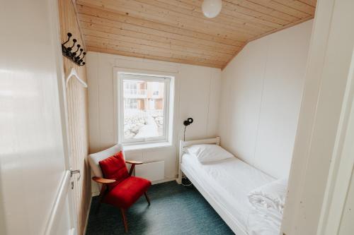 a small room with a bed and a red chair at Hemmingodden Lodge in Ballstad