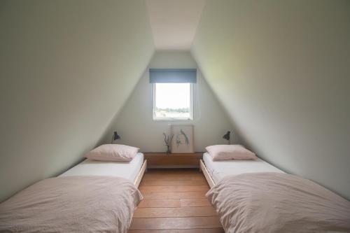 two beds in a attic room with a window at Hermans huisje: het mooiste uitzicht van Twente? in Haaksbergen