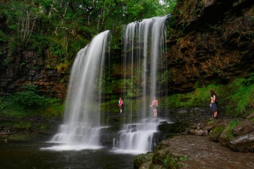 two people standing in front of a waterfall at Waterfall Lodge in Pont-Nedd-Fechan
