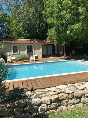 a swimming pool with a wooden deck next to a house at L'atelier des Coudelières in Le Thor