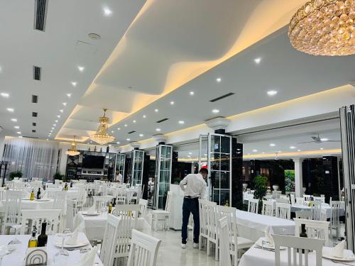 a man standing in a restaurant with white tables and chairs at Ujvara Hotel in Golem