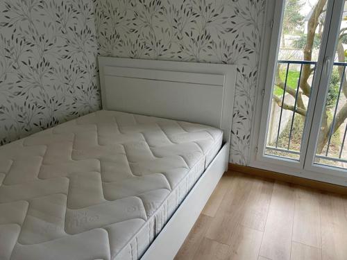 een wit bed in een kamer met een raam bij Appartement de deux chambres au calme in Nozay