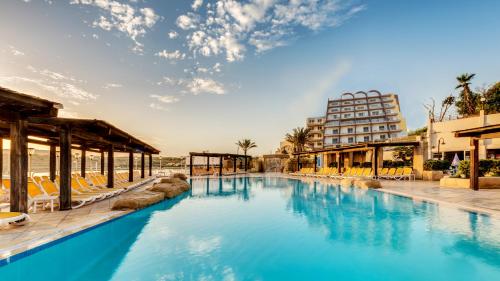 una piscina in un resort con sedie e un edificio di AX Sunny Coast Resort & Spa a San Pawl il-Baħar