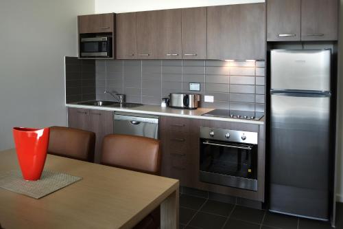 eine Küche mit einem Kühlschrank aus Edelstahl und einem Holztisch in der Unterkunft Quest Palmerston - Darwin in Darwin