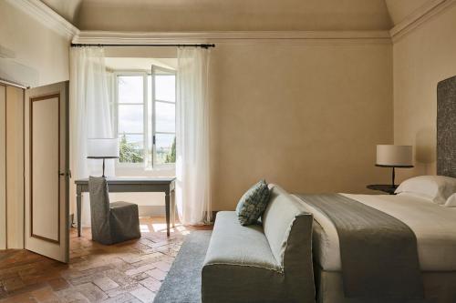 a bedroom with a bed and a chair and a window at COMO Castello Del Nero in Tavarnelle in Val di Pesa