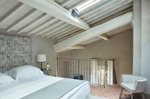 a bedroom with a white bed and a chair at COMO Castello Del Nero in Tavarnelle in Val di Pesa