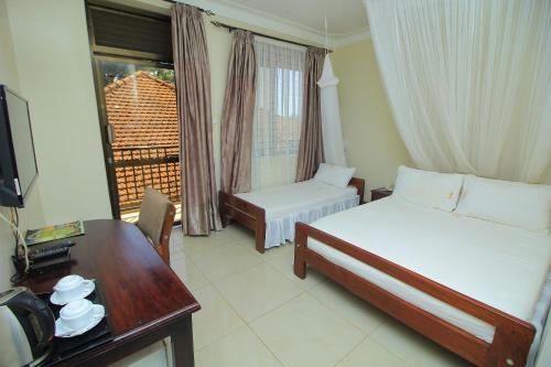 a bedroom with two beds and a desk and a window at Al-Nisaa Hotel and Spa in Jinja