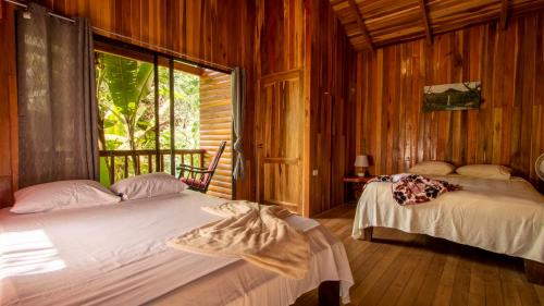 two beds in a room with wooden walls and a window at Arenal Rústic Lodge in Fortuna
