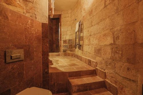 a bathroom with a toilet and a stone wall at Sinasos Palace Cave Hotel in Urgup