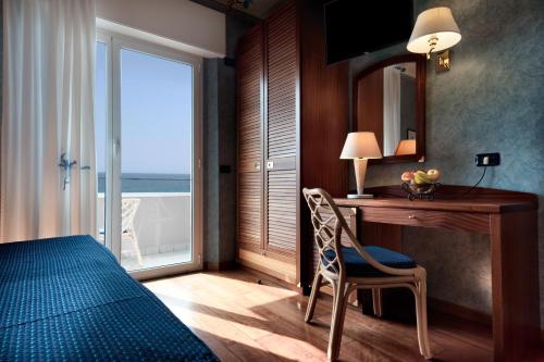 a bedroom with a bed and a desk and a window at Hotel Atilius & Suites in Riccione
