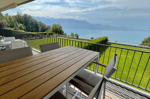 a balcony with a wooden table and chairs and the ocean at Les Terrasses de Lavaux 1 - Appartement de luxe avec vue panoramique et piscine in Puidoux