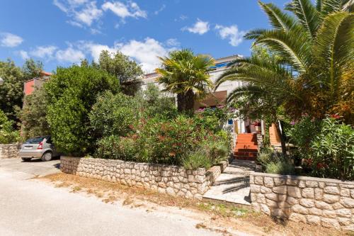 a house with a stone wall and a palm tree at Apartments Nives, Artatore in Mali Lošinj