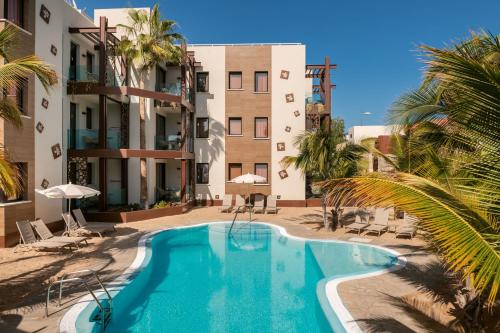 a swimming pool in front of a building with palm trees at Alhambra Boutique Apartments by TAM Resorts in Playa del Ingles