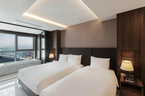 two beds in a hotel room with a large window at Hotel Adela in Busan
