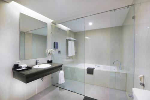 a bathroom with a sink and a tub and a mirror at Harper Perintis by ASTON in Makassar