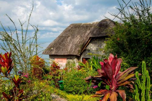 an old house with a thatched roof in a garden at Hakuna Matata Lodge in Gisenyi