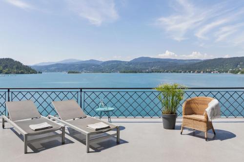 a balcony with two chairs and a table and water at Hotel Linde in Maria Wörth