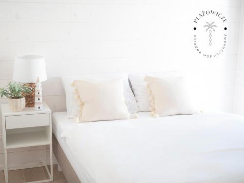 ein weißes Schlafzimmer mit einem Bett mit weißen Kissen in der Unterkunft PLAŻOWICZE - domki letniskowe w Mielnie in Mielno