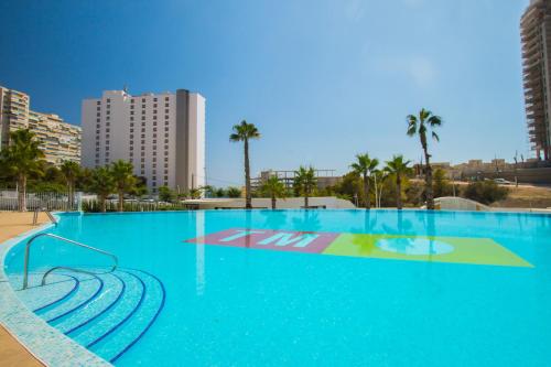 a large swimming pool with blue water and palm trees at Waves apartment - relax in Costa Blanca in Benidorm