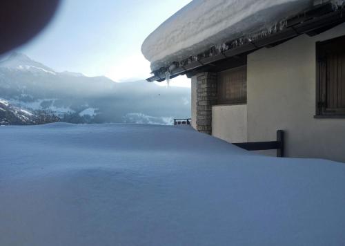 un techo cubierto de nieve de un edificio con montañas en el fondo en Gli appartamenti della Fra en Torgnon