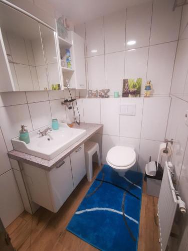 a bathroom with a sink and a toilet and a blue rug at Pension & Apartments Linkemühle in Niederfell