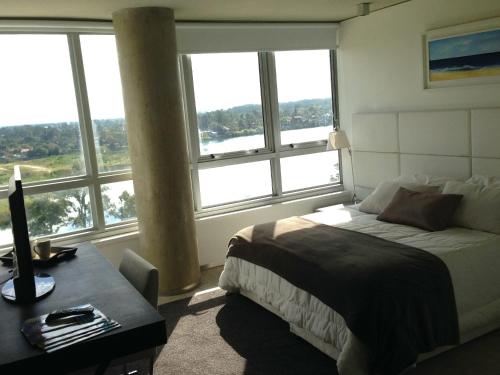 um quarto com uma cama, uma secretária e janelas em Faros de Carrasco Apartments em Montevidéu