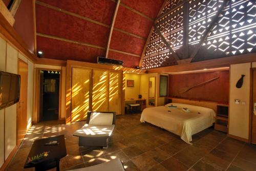 a bedroom with a bed and a chair in a room at Maitai Lapita Village Huahine in Fare