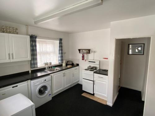 a kitchen with white cabinets and a washer and dryer at Cosy 1-bedroom cottage with indoor open fireplace in Westgate