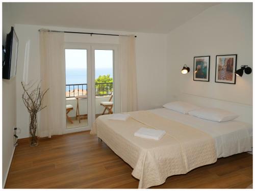 a white bedroom with a bed and a balcony at Apartmani Makelja in Primošten