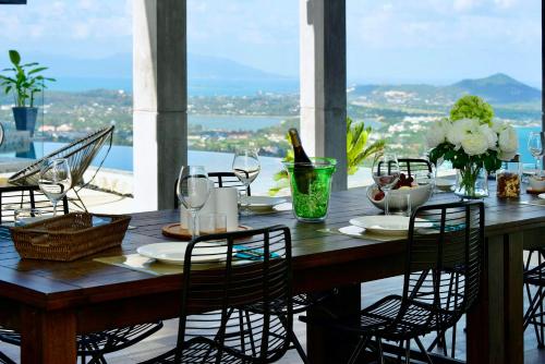 a wooden table with chairs and a table with wine glasses at Paradise Villa Elysium - Sea View Infinity Pool with Waterfall & Jacuzzi in Koh Samui 