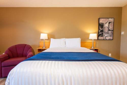 a bedroom with a large bed and two chairs at Ocean Crest Motel in Qualicum Beach