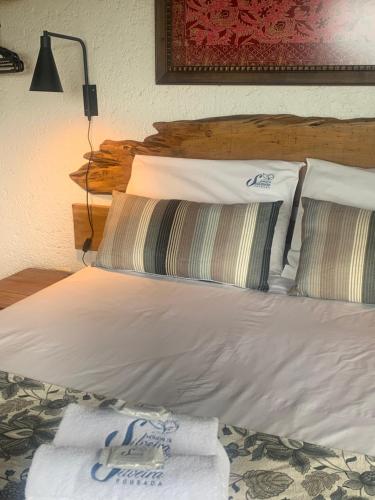 uma cama com lençóis brancos e almofadas num quarto em Pousada Moradas da Silveira em Garopaba