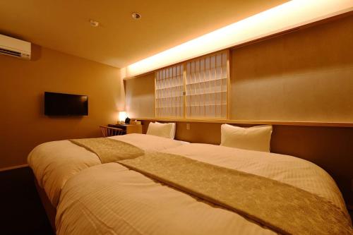 two beds in a hotel room with a window at Kyoyado Heianshiki in Kyoto
