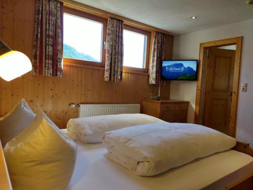 a bedroom with two beds and a tv and two windows at Pension Edelweiss in Damuls