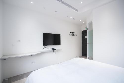 a white bedroom with a bed and a tv on the wall at The Way Inn in Taichung