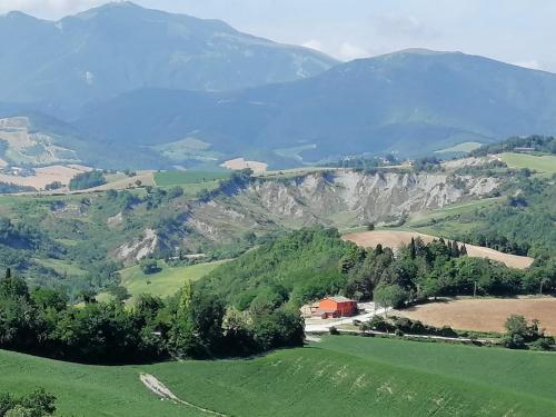a green hillside with a barn and mountains in the background at A casa di Matisse - appartamento vacanze in Urbino