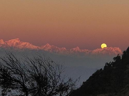 a sunset with the moon over the mountains at The Bugyal in Kanatal