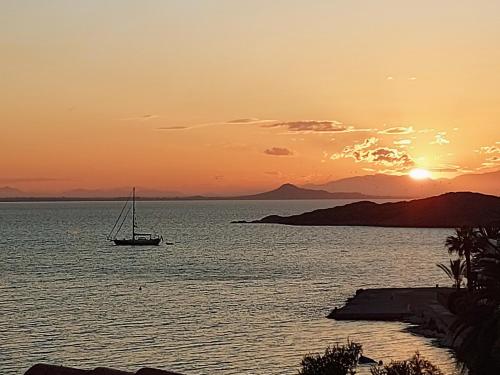 un barco en el agua con la puesta de sol en el fondo en NIDO DEL AMOR deluxe 1a linéa Terraza Indoorpool Wifi Aire Netflix 10 metros a Cala del Pino en La Manga del Mar Menor