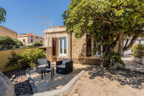a house with two chairs and a table and a tree at Villa Mosca Charming House in Alghero