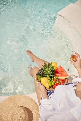 a woman sitting next to a pool with a plate of fruit at Hotel Admiral in Budva
