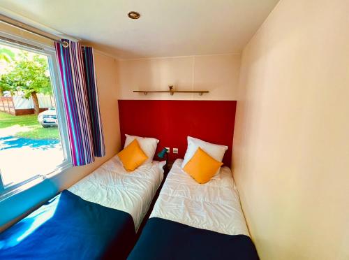 Duas camas num pequeno quarto com uma janela em Cosy Lili - Mobilhome MANDARINE - Proche océan em Saint-Georges-de-Didonne