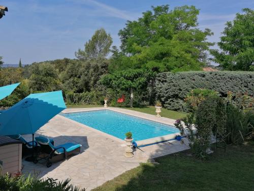 a swimming pool in a yard with a blue umbrella at Hôtes'Antic Provence in Lorgues