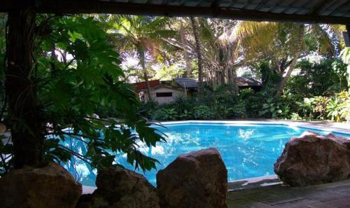 a blue swimming pool with trees and a house at Posada El Jardin in Ticul