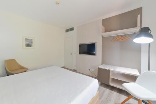 a white bedroom with a bed and a desk and a tv at Hotel Baia Delle Sirene in Taormina