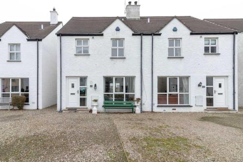 a white house with a green bench in front of it at Strand Cottages Ballycastle Seafront in Ballycastle