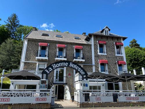 un gran edificio de piedra con sombrillas delante en Hôtel-restaurant La bonne hôtesse, en Chambon-sur-Lac